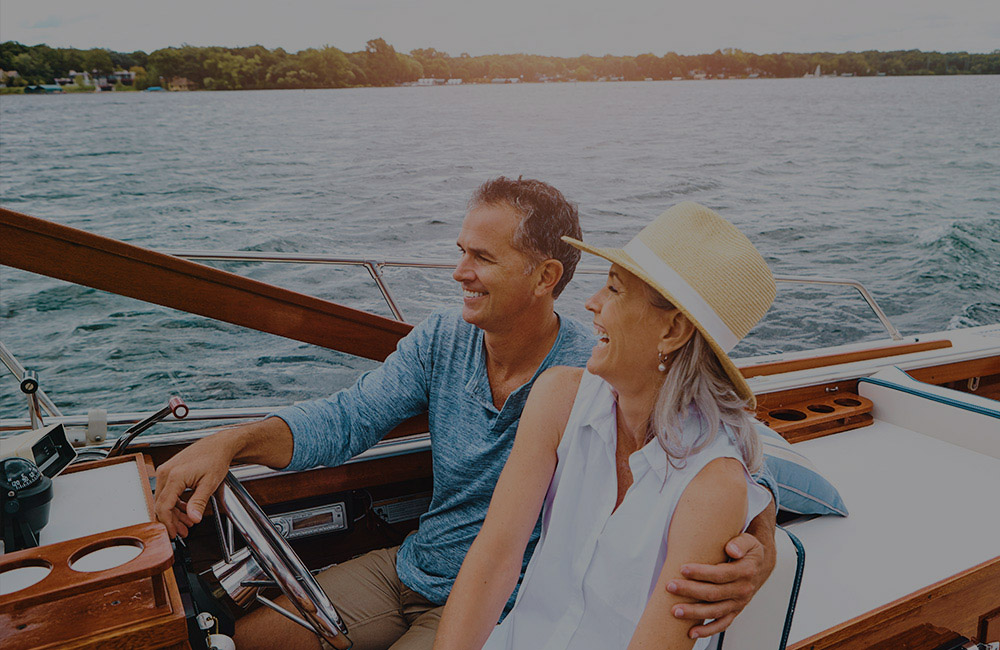 A man and woman in a boat - he has his arm wrapped around her shoulder are they laugh together